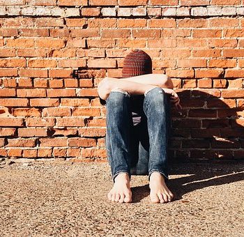 Junger Mann sitzt mit gesenktem Kopf auf dem Boden