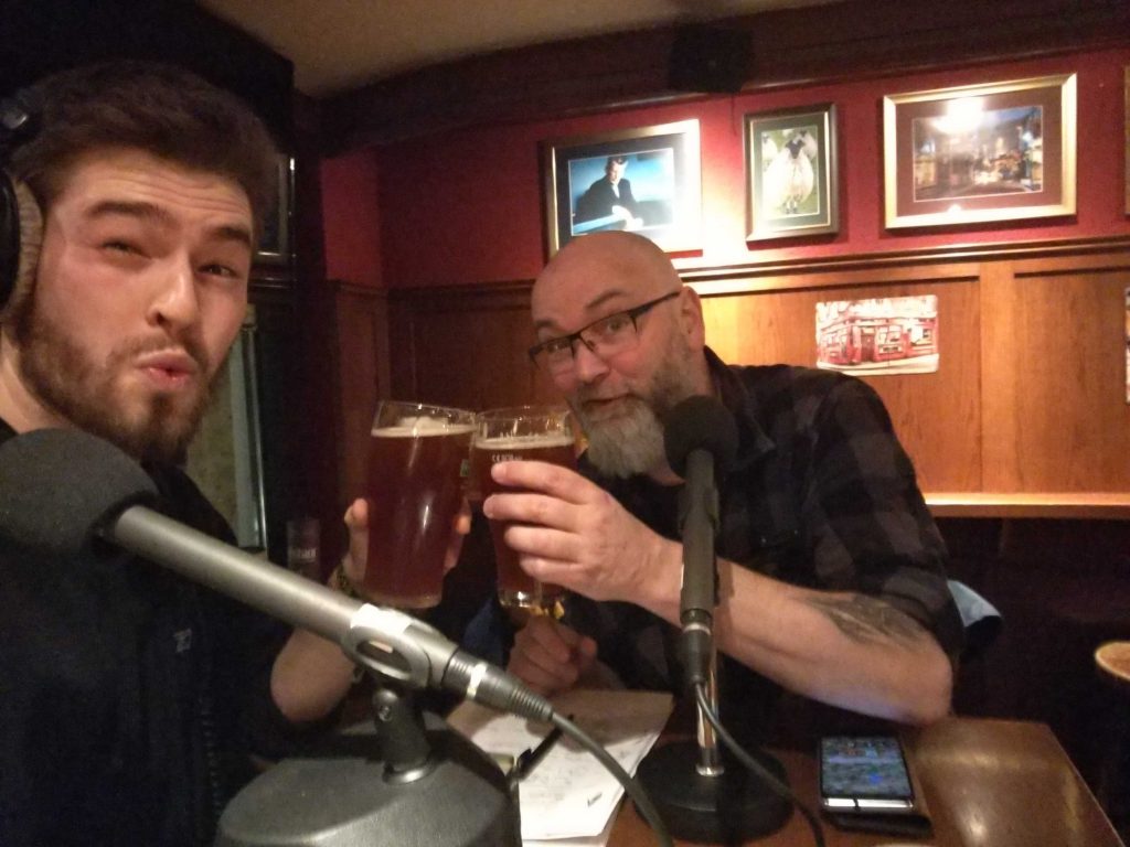 Redakteure Matz und Chris mit zwei Gläsern Bier und Aufnahmemikrofonen in einem Pub