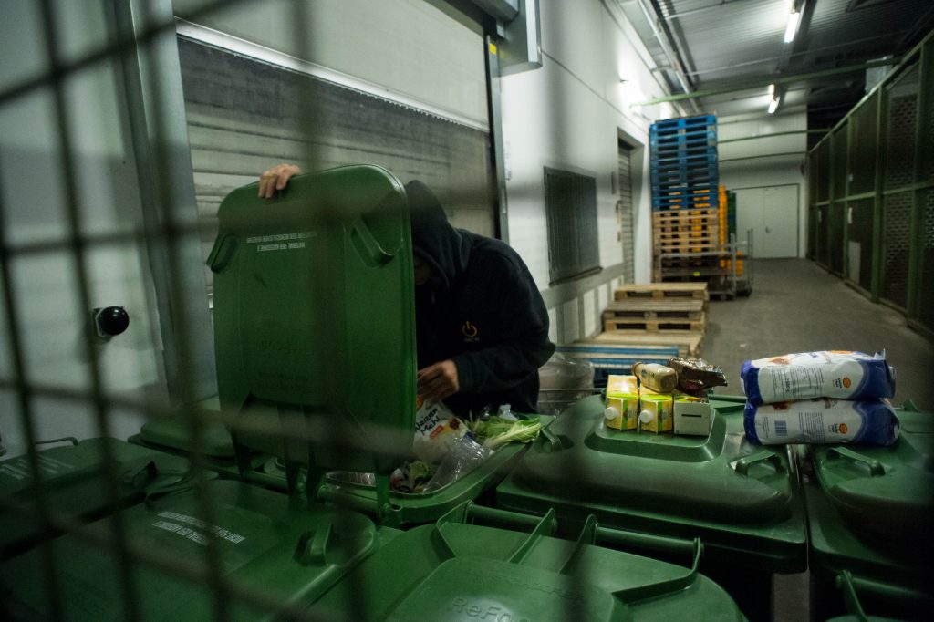 Junger Mann holt Lebensmittelpackungen aus einer großen Mülltonne