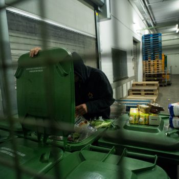 Junger Mann holt Lebensmittelpackungen aus einer großen Mülltonne