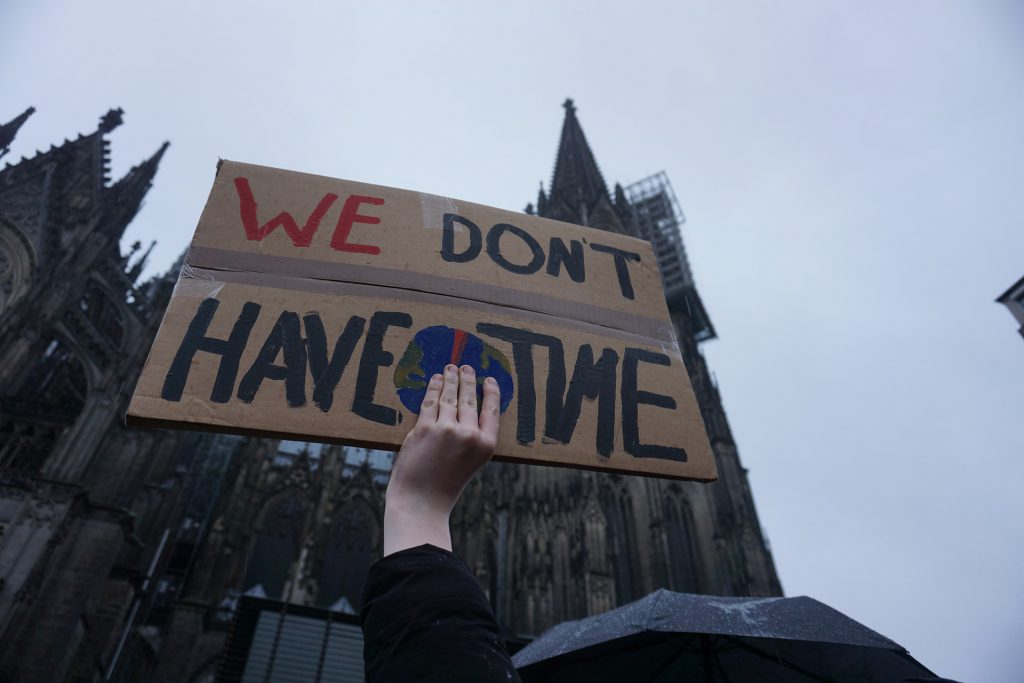 Aktivist hält Pappschild vor Kölner Dom hoch mit Aufschrift "We don't have time"