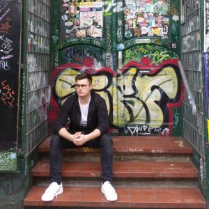 junger Mann sitzt auf einer Treppe vor einer Tür mit Graffiti