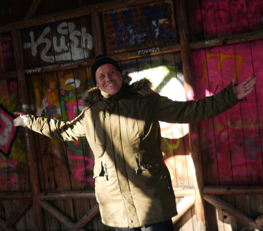 Mann steht mit ausgestreckten Armen vor Wand mit Graffiti