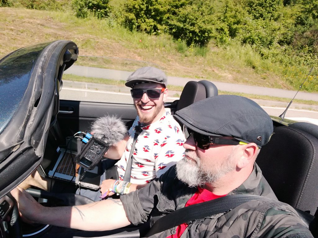 Zwei Männer im fahrenden Cabrio mit Tonaufnahmegerät