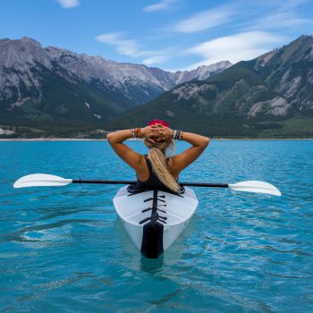 Frau im Kajak auf einem See mit Blick auf Berge