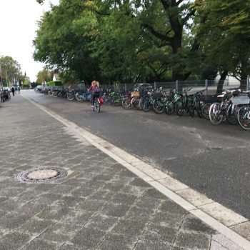 Straße, daneben ein Bürgersteig, auf dem viele Fahrräder geparkt sind