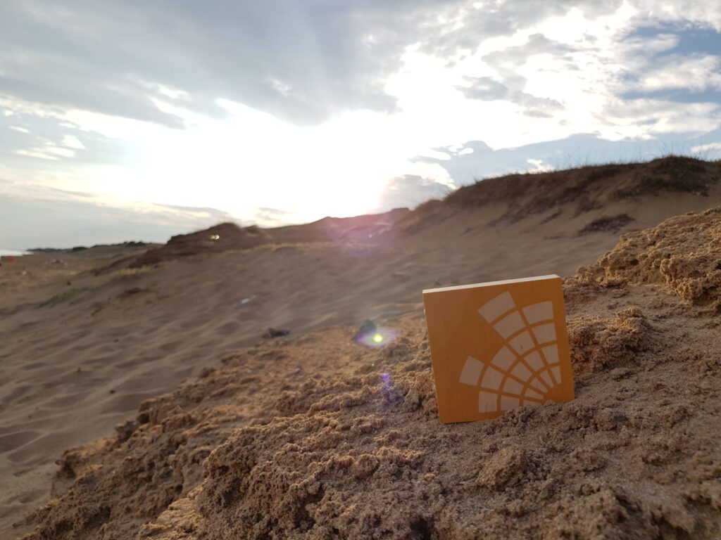 Holztafel mit Campusradio-Logo steckt in einem Berg von Sand