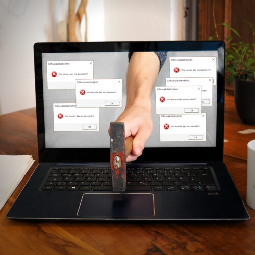 Laptop, aus dessen Bildschirm eine Hand mit Hammer ragt, die auf die Tastatur haut